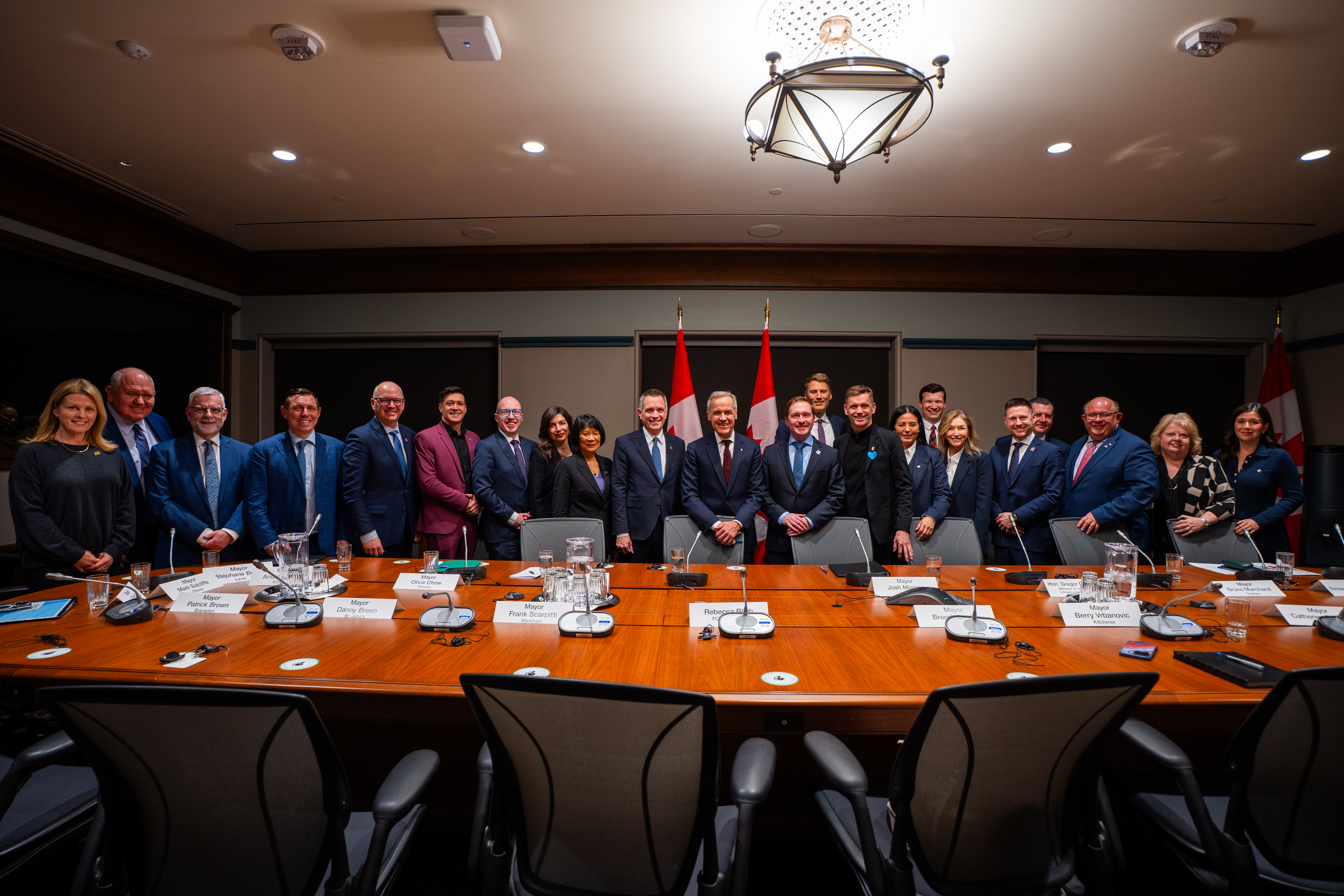 A large group of people in business attire stand together at the front of a formal meeting room behind a long conference table