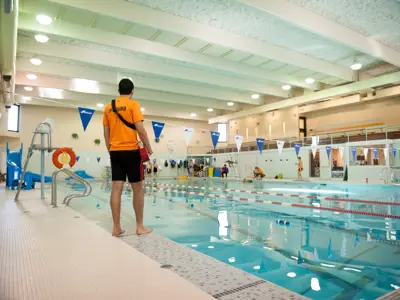 lifeguard standing at edge of pool with swimmers swimming